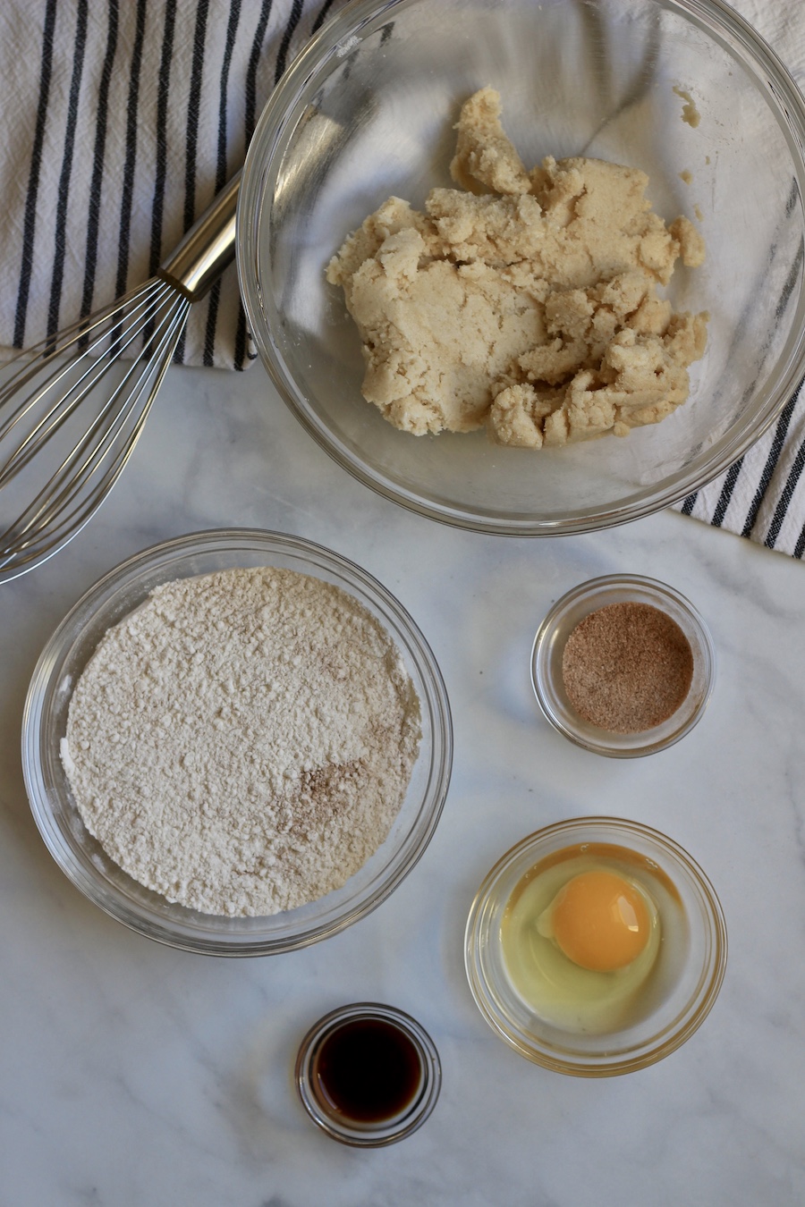 The ingredients in glass bowls on a marble backdrop with a wire whisk.