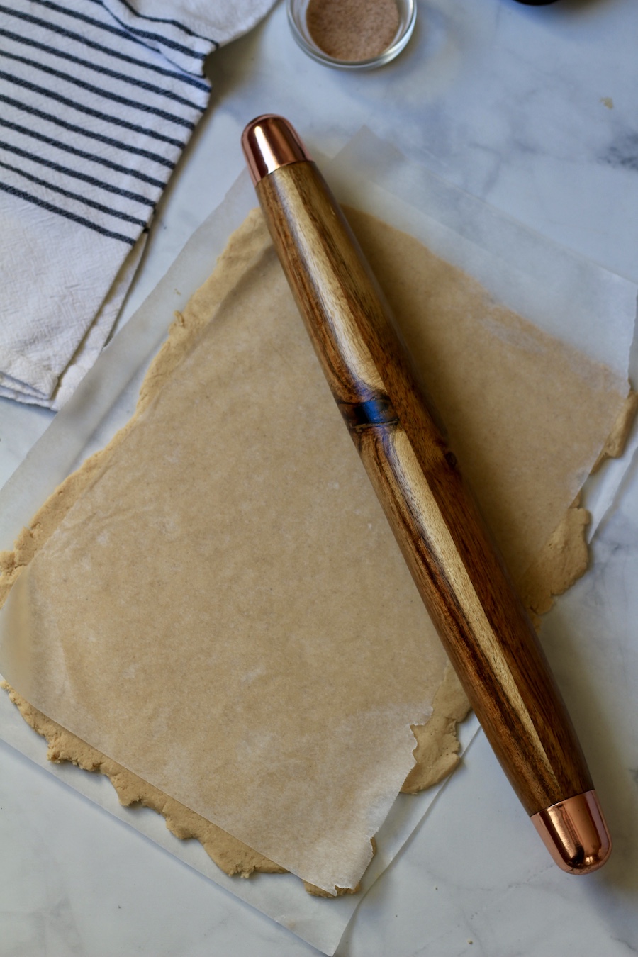 A rolling pin pressing out the dough for snickerdoodle cookies on parchment paper.
