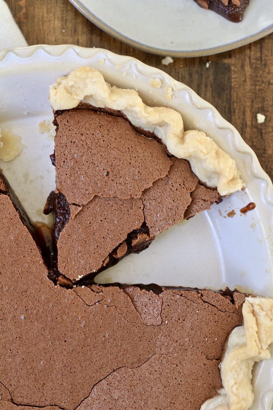 A close up shot of a slice of chocolate chess pie in a pie pan on a wooden counter.