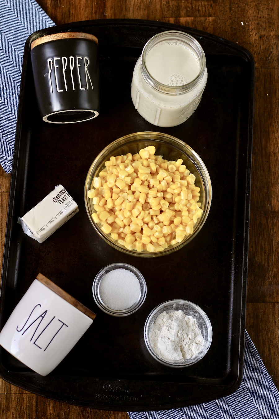 Ingredients for vegan creamed corn recipe on a rimmed cookie sheet on wooden counter.
