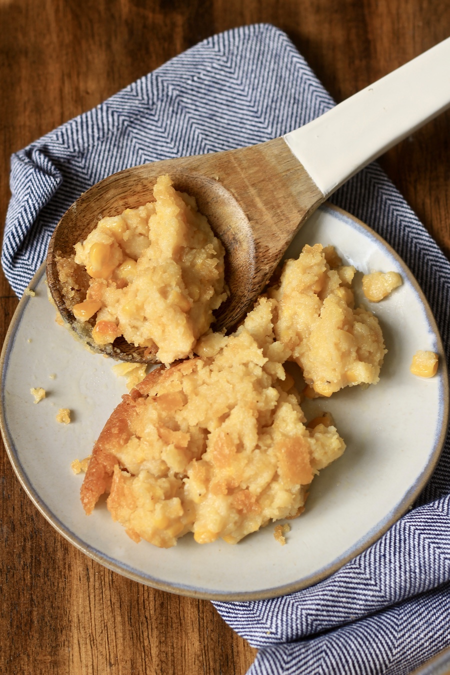 A small plate of corn casserole with a wooden spoon on a blue towel.