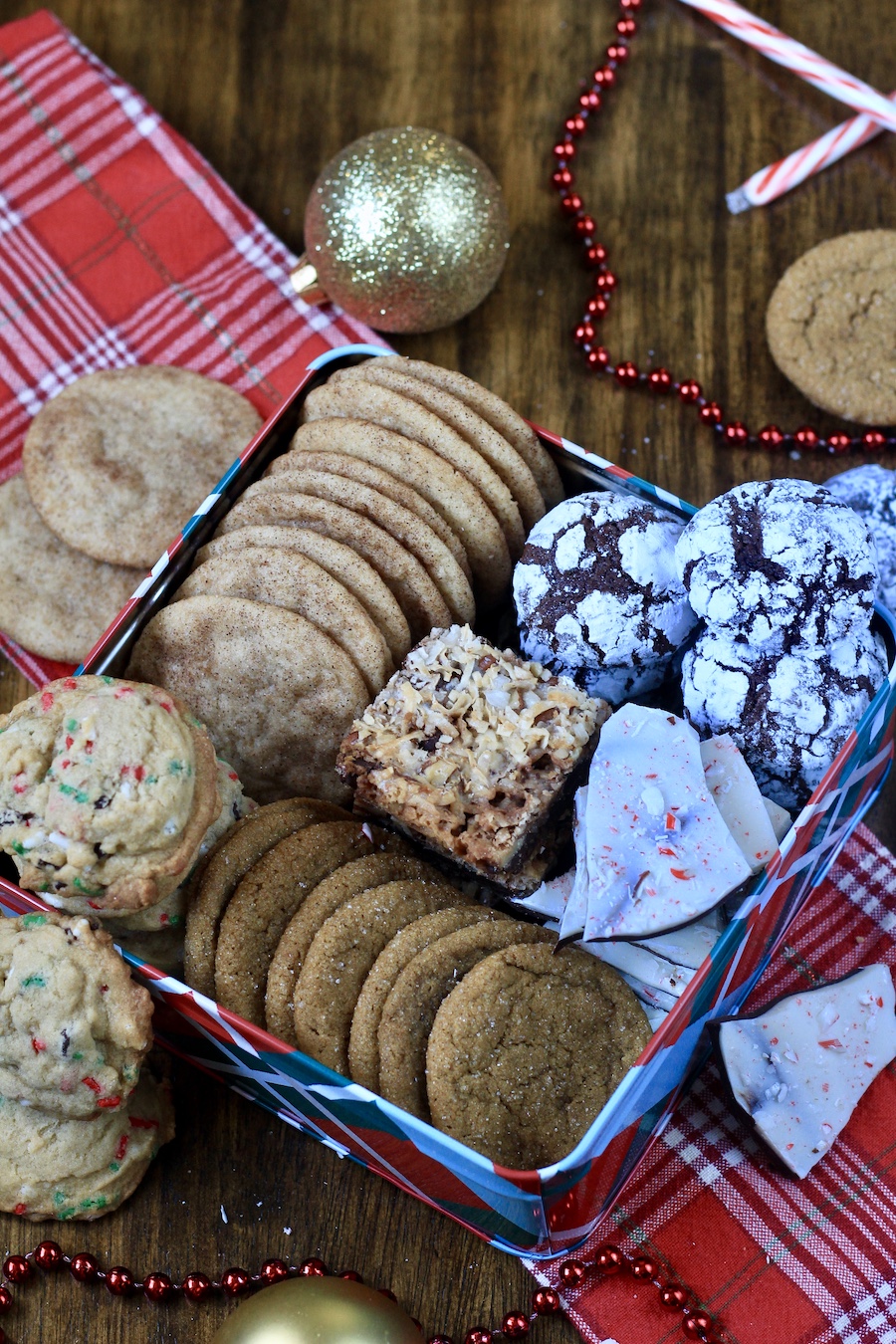 A holiday cookie box packed with dairy free cookies on a plaid dish towel with a gold ornament in the back.
