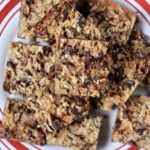 A red and white plate with square magic cookie bars stacked on top on a white and red towel.
