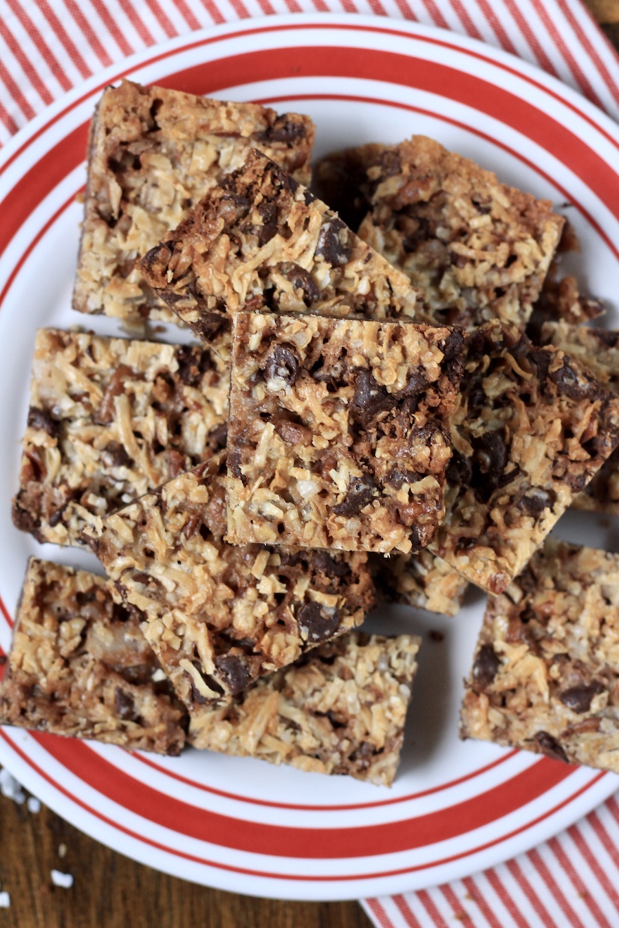 A red and white plate with square magic cookie bars stacked on top on a white and red towel.