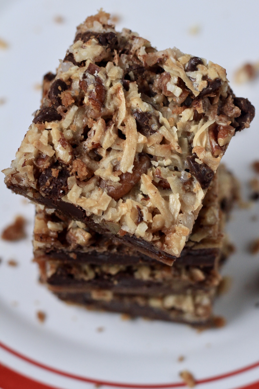 A stack of four magic cookie bars on a white plate with a red rim.