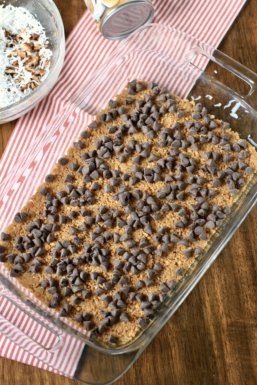 Chocolate chips on top of a graham cracker crust in a baking dish on a red and white striped dish towel.