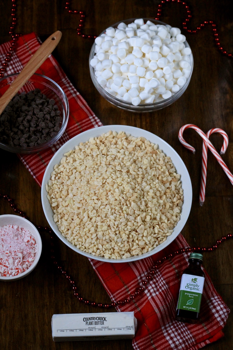 Ingredients for peppermint bark rice krispie treats on a wooden table with a red dish towel.