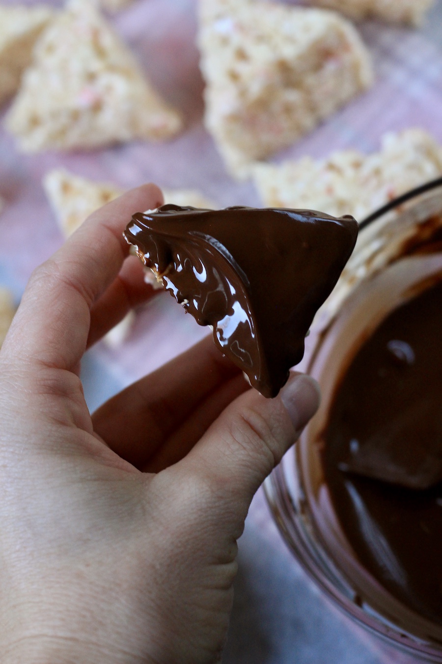 A single rice krispie dipped in peppermint chocolate with a hand holding it.