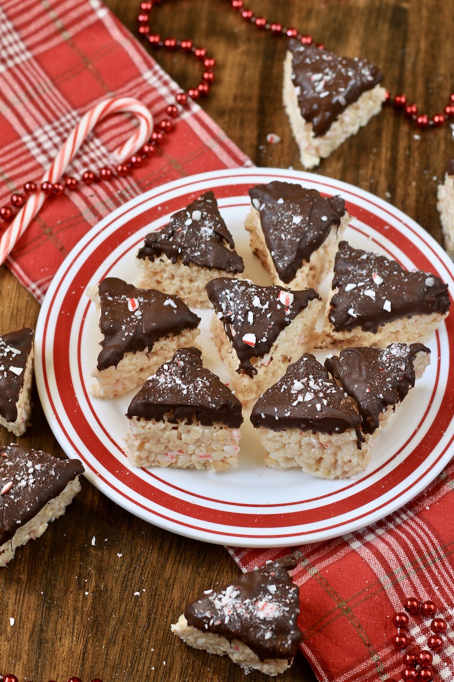 A red rimmed plate with peppermint bark rice krispie treats on a red towel with candy canes in the back.