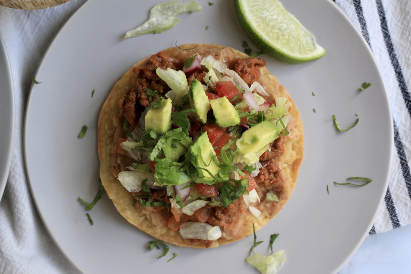 An oven baked beef tostada on a white plate with a lime wedge.