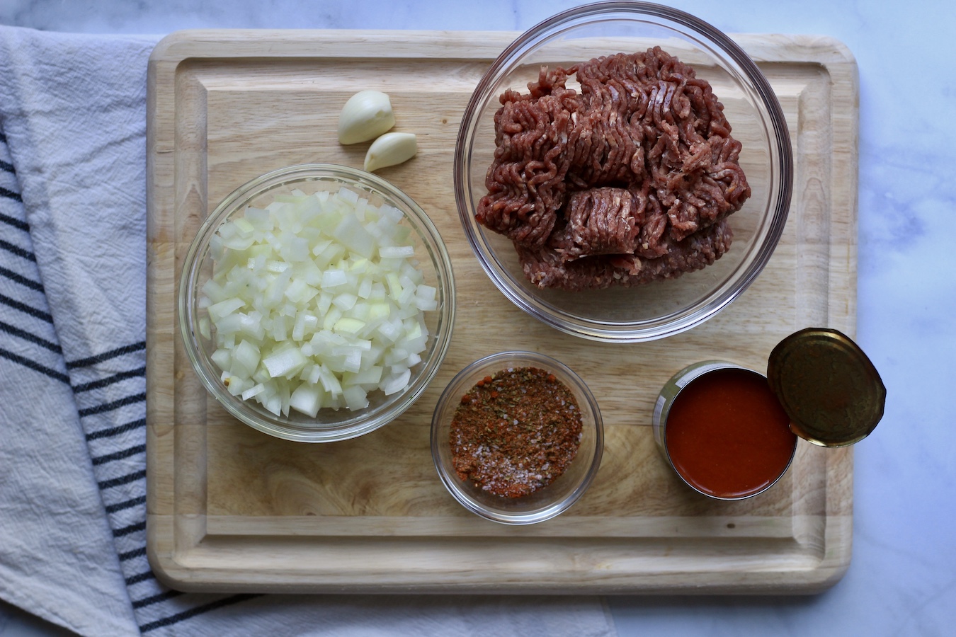 A wooden cutting board with the ingredients for beef taco meat.