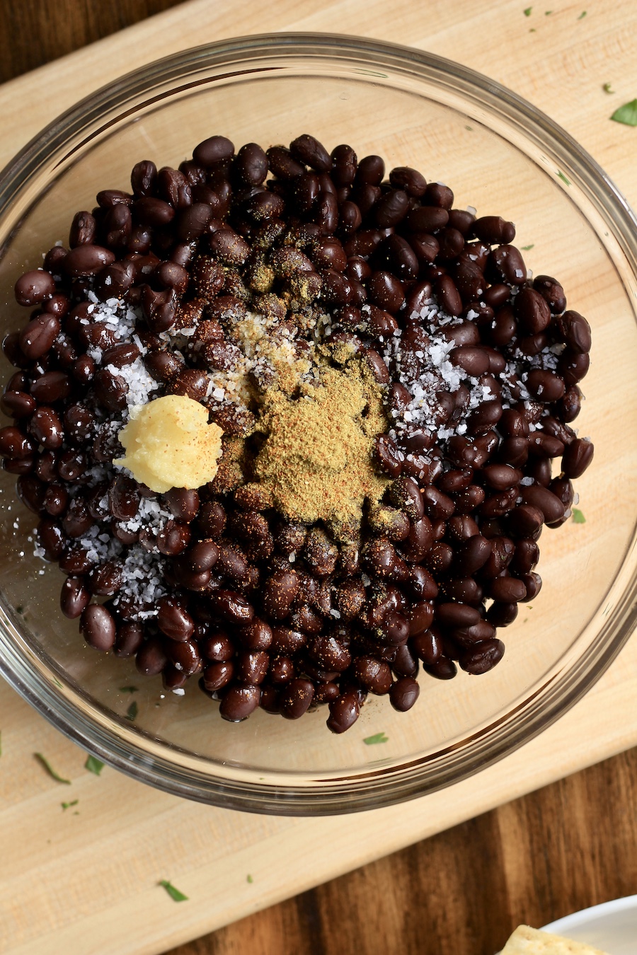 A bowl with black beans, spices, garlic on a wooden counter.