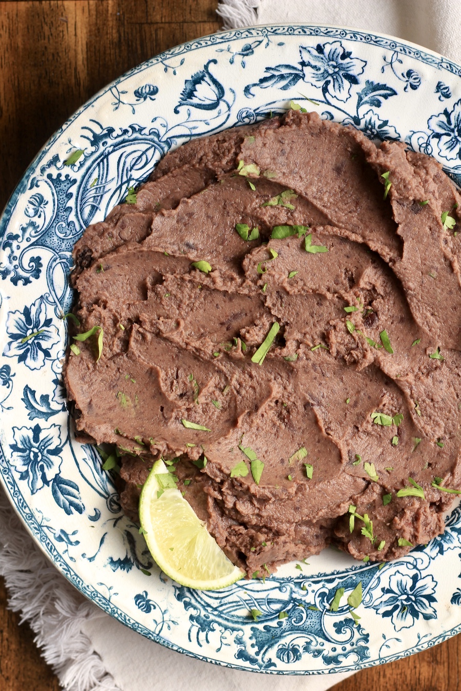 A black bean dip topped with a lime wedge in a blue and white bowl on a white towel.