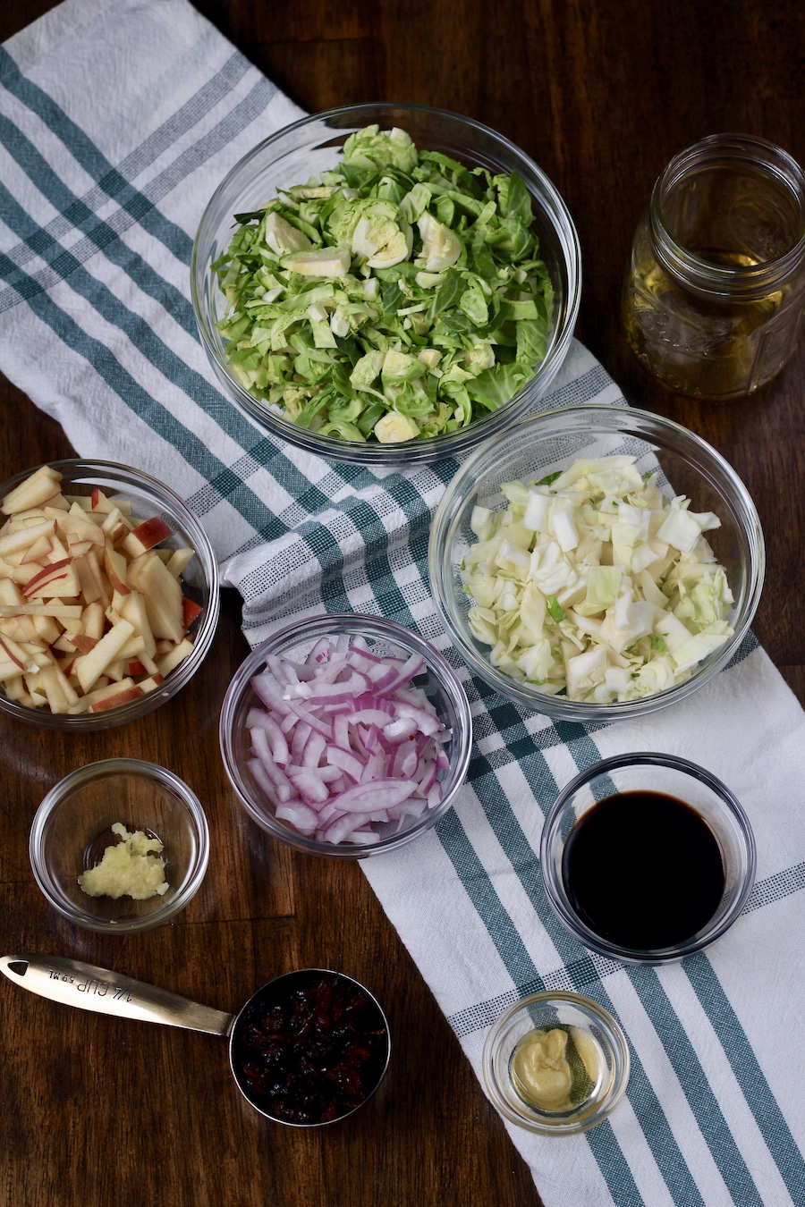 Ingredients for brussels sprouts salad chopped and in glass bowls on a wooden counter.