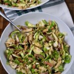 A serving bowl with brussels sprouts salad with a fork in the top on a white and green dish towel.