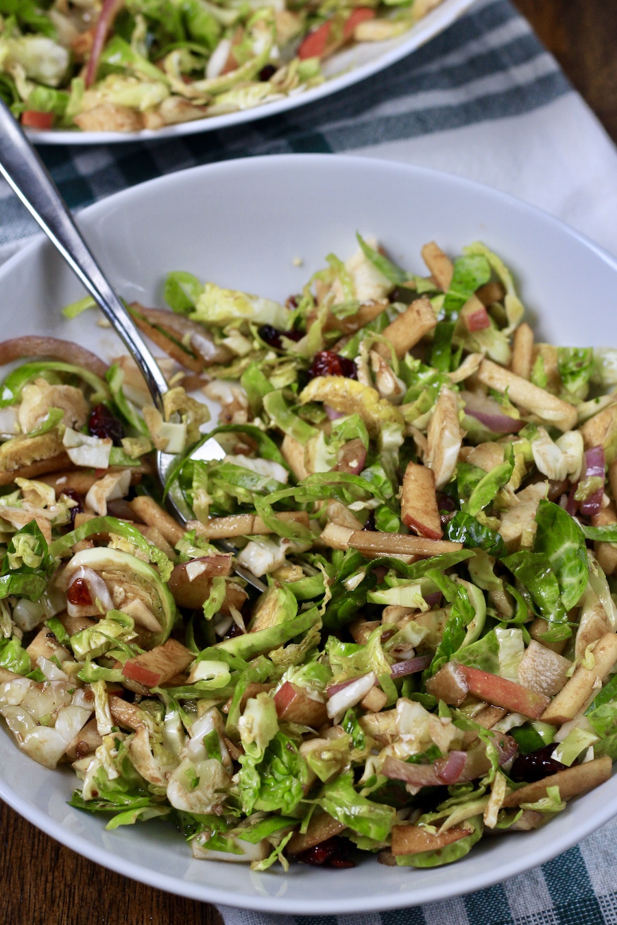 A small bowl of brussels sprouts salad with a silver fork on a white and green dish towel.