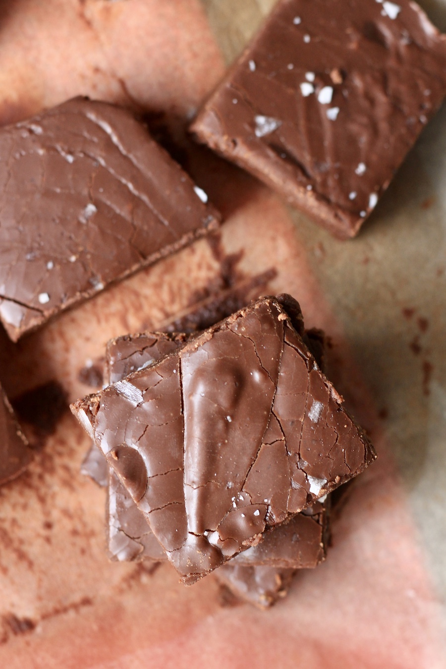 A stack of chocolate fudge with sea salt on parchment paper.