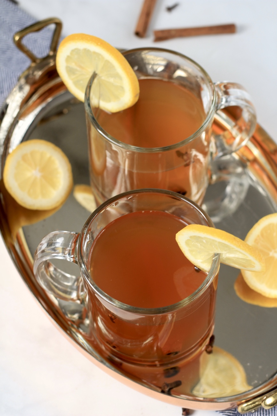 Two glass mugs with hot toddies and lemon slices on the rim and lemon ends in the copper tray.
