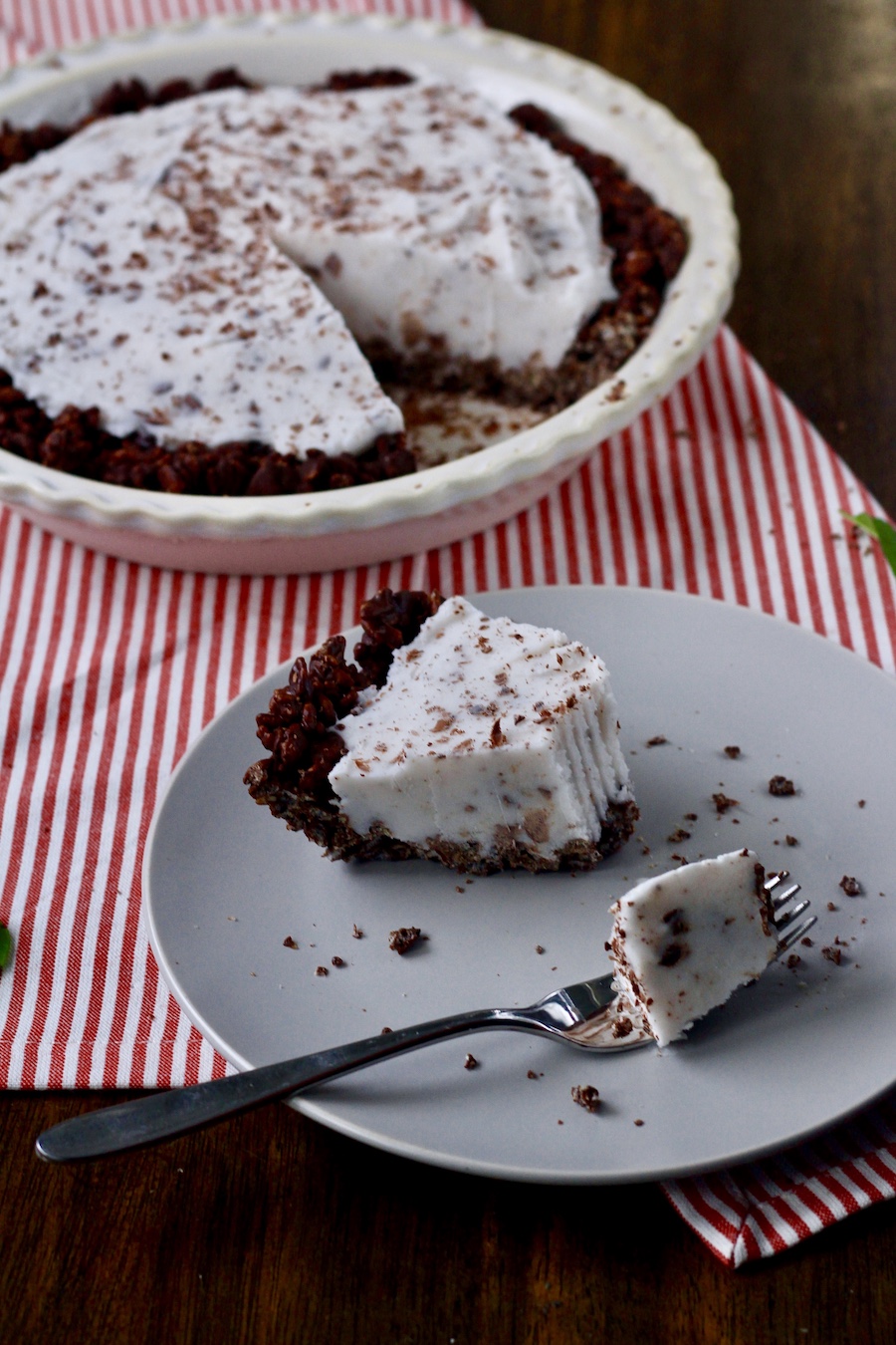 A slice of mint ice cream pie on a white plate with a fork that has taken a bite out with a pie in the back.