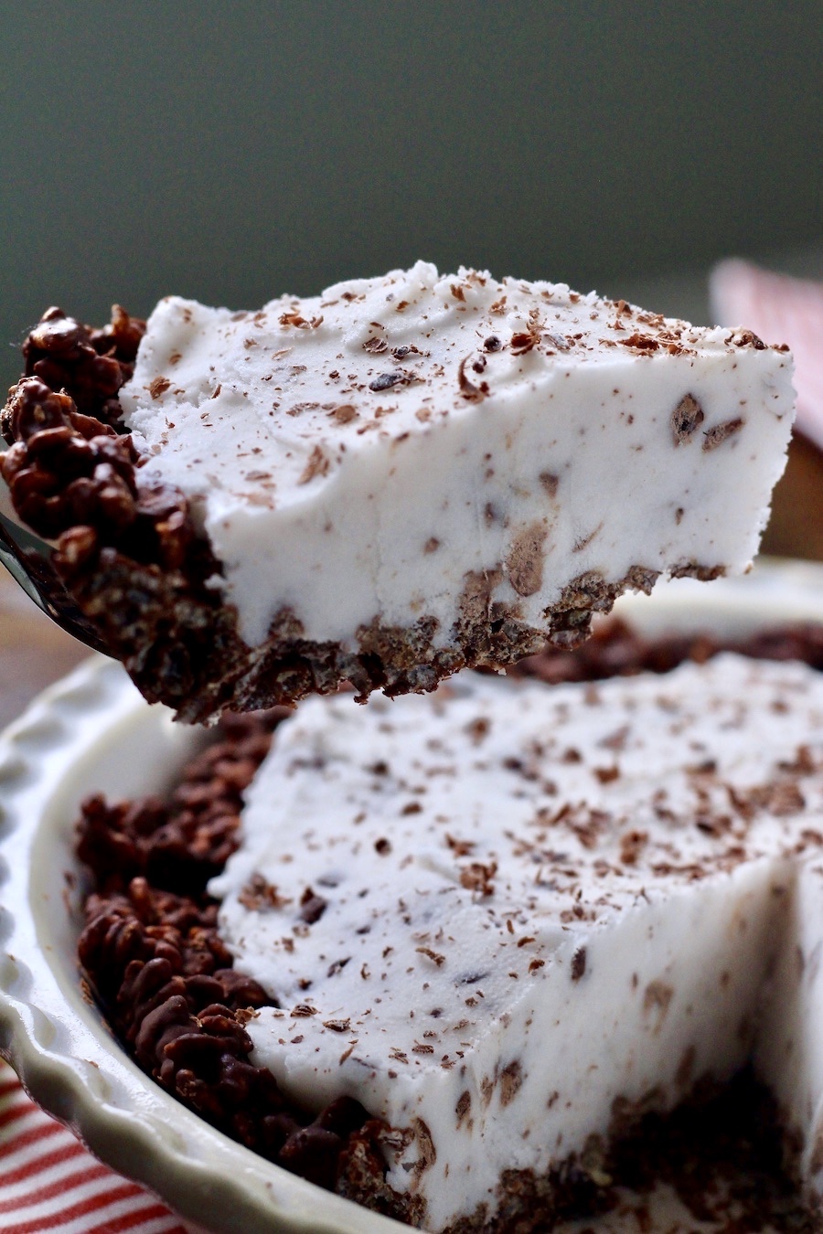A slice of mint ice cream pie being held above a full ice cream pie.