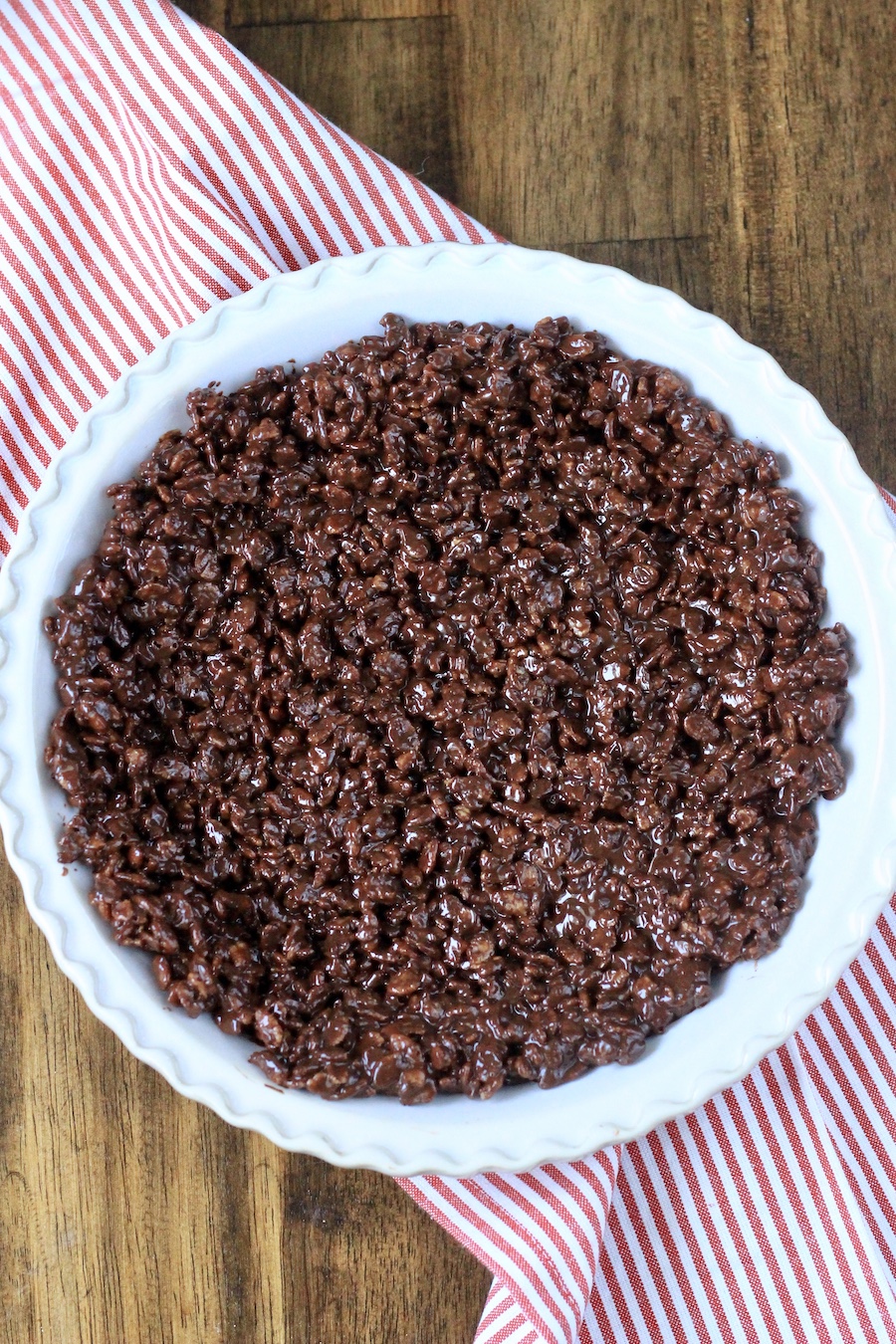 A pie pan with the chocolate krispie crust before freezing on a red and white striped towel.