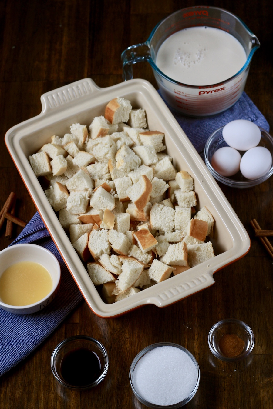 The ingredients for vanilla bread pudding on a wooden table with a blue towel.