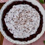 A full mint ice cream pie with a chocolate crust in a pie pan with a white and red striped towel.