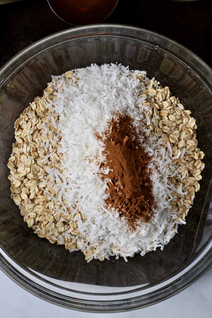 A glass bowl with old-fashioned oats, coconut shreds, and cinnamon.