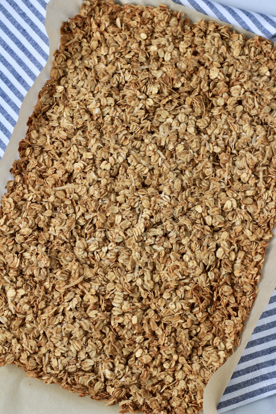 Coconut granola on a piece of parchment paper on top of blue and white striped towel.