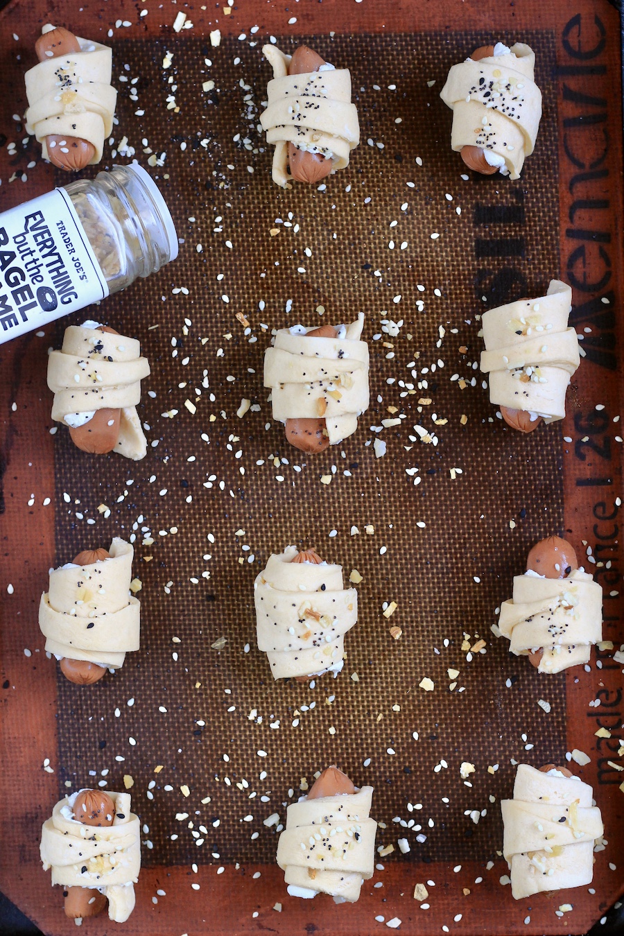 everything bagel pigs in a blanket on a baking sheet with a jar of everything bagel seasoning.