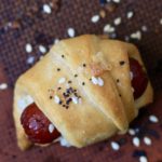 One baked everything bagel pigs in a blanket on a baking sheet.