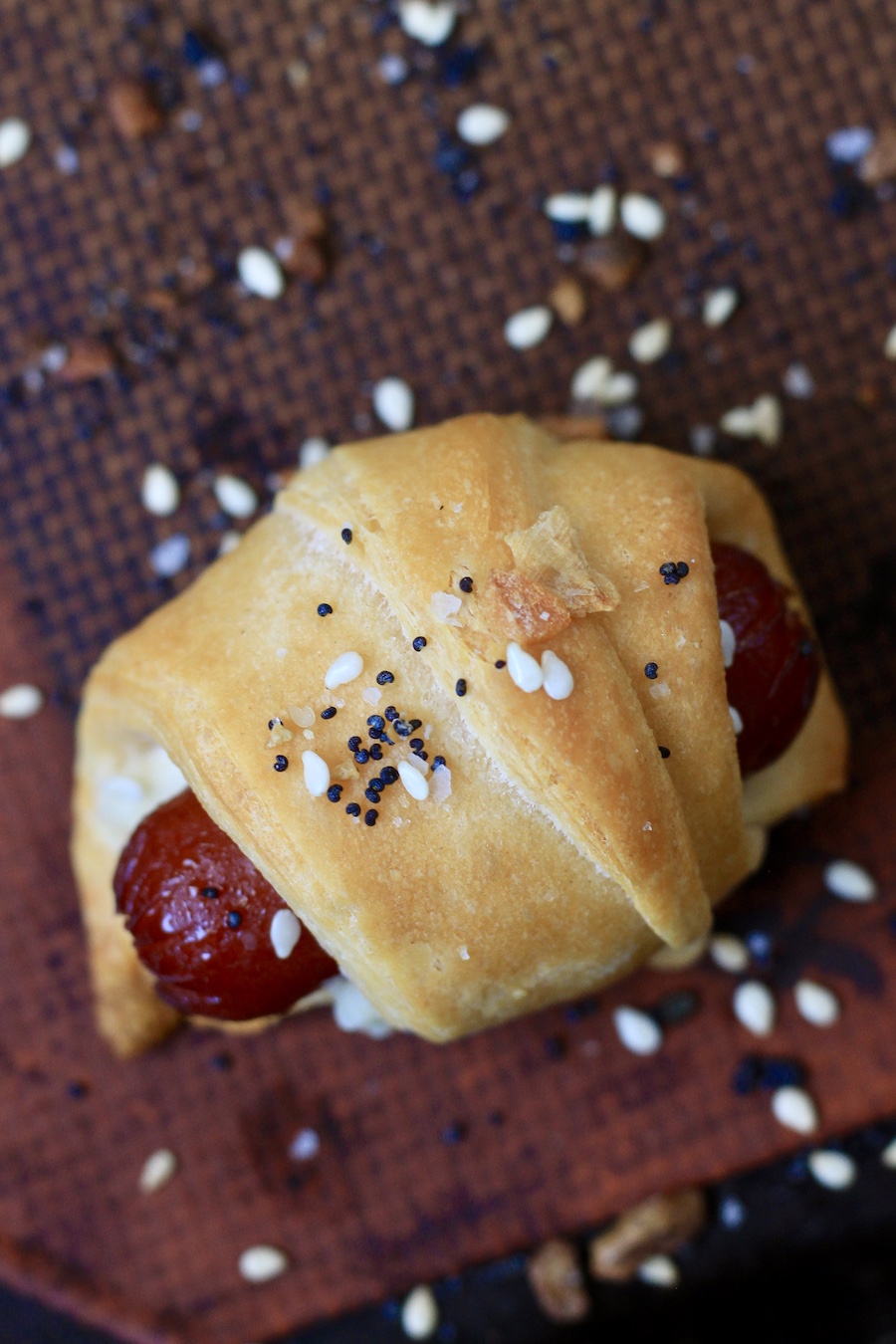 One baked everything bagel pigs in a blanket on a baking sheet.
