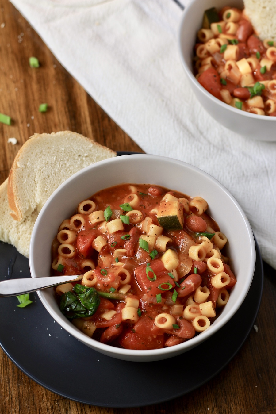 A blue plate with a white bowl filled with minestrone soup on top and a white dish towel in back.