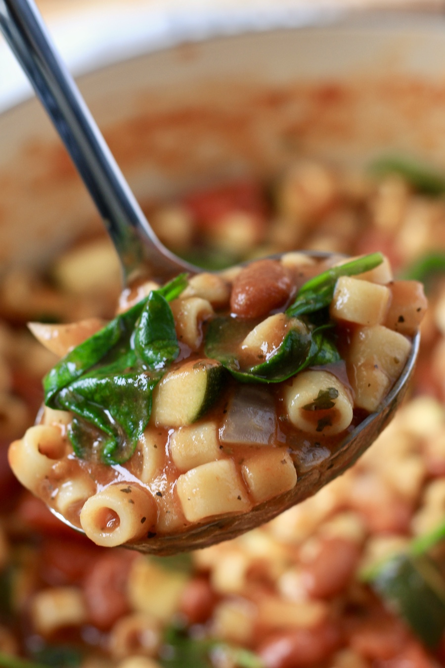 A silver spoon with a scoop of minestrone soup over a pot of minestrone soup.