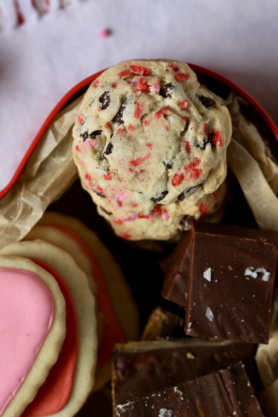 A valentine's day monster cookie in the top right corner of the dessert box with cookies and fudge near by.