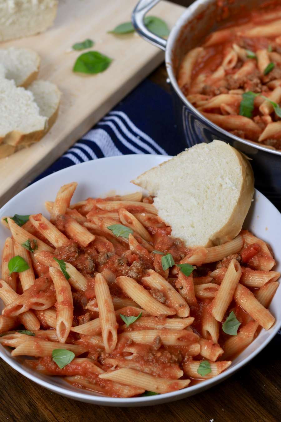 A bowl of Arrabbiata meat sauce and pasta with a slice of bread on the right.