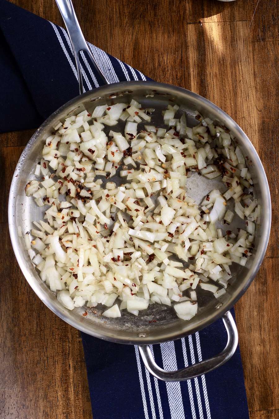 A skillet with onion and garlic on a blue towel on a wooden counter.