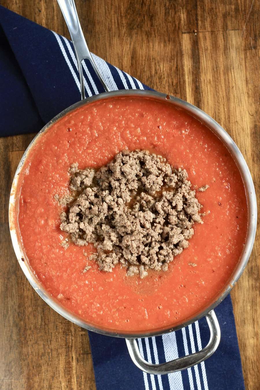 Spicy meat sauce in a skillet on a blue towel on a wooden counter.