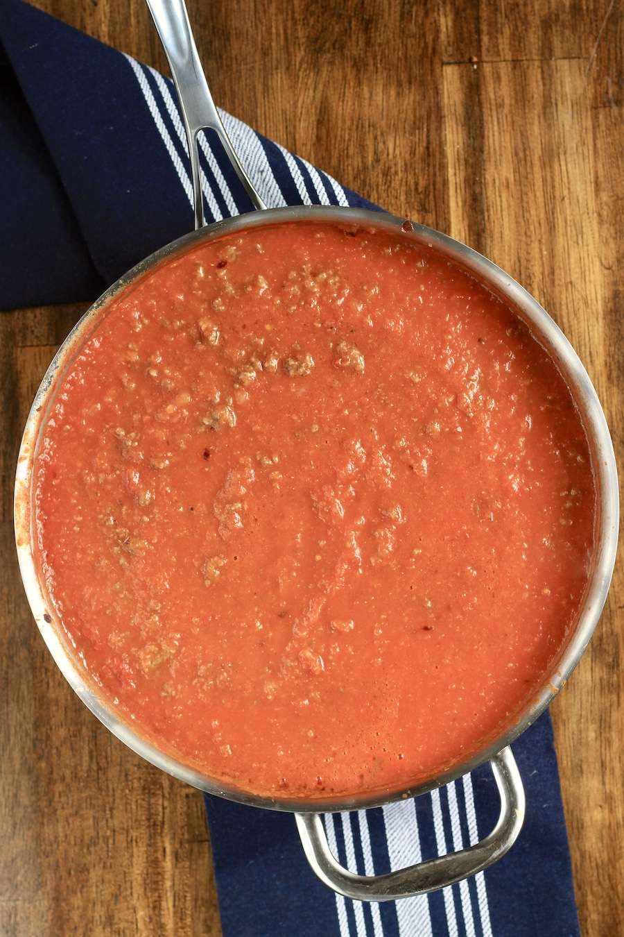 Arrabbiata meat sauce in a skillet on a blue towel on a wooden counter.