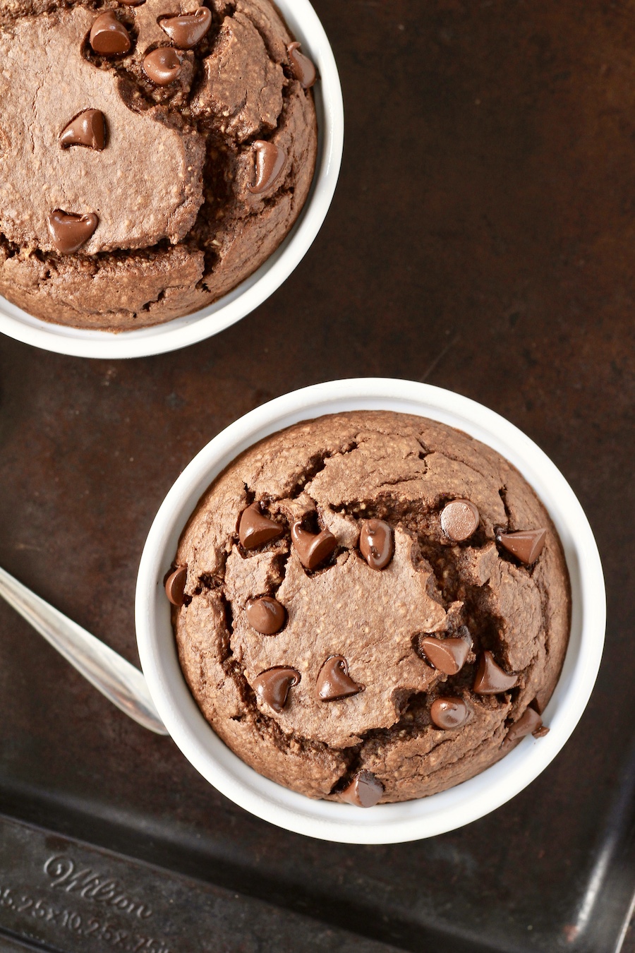 Chocolate baked oats in white ramekins on a baking sheet with a spoon to the left.