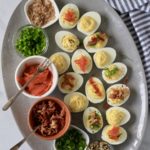 A top down photo of the whole deviled egg platter with toppings on the left and different deviled eggs on the right.