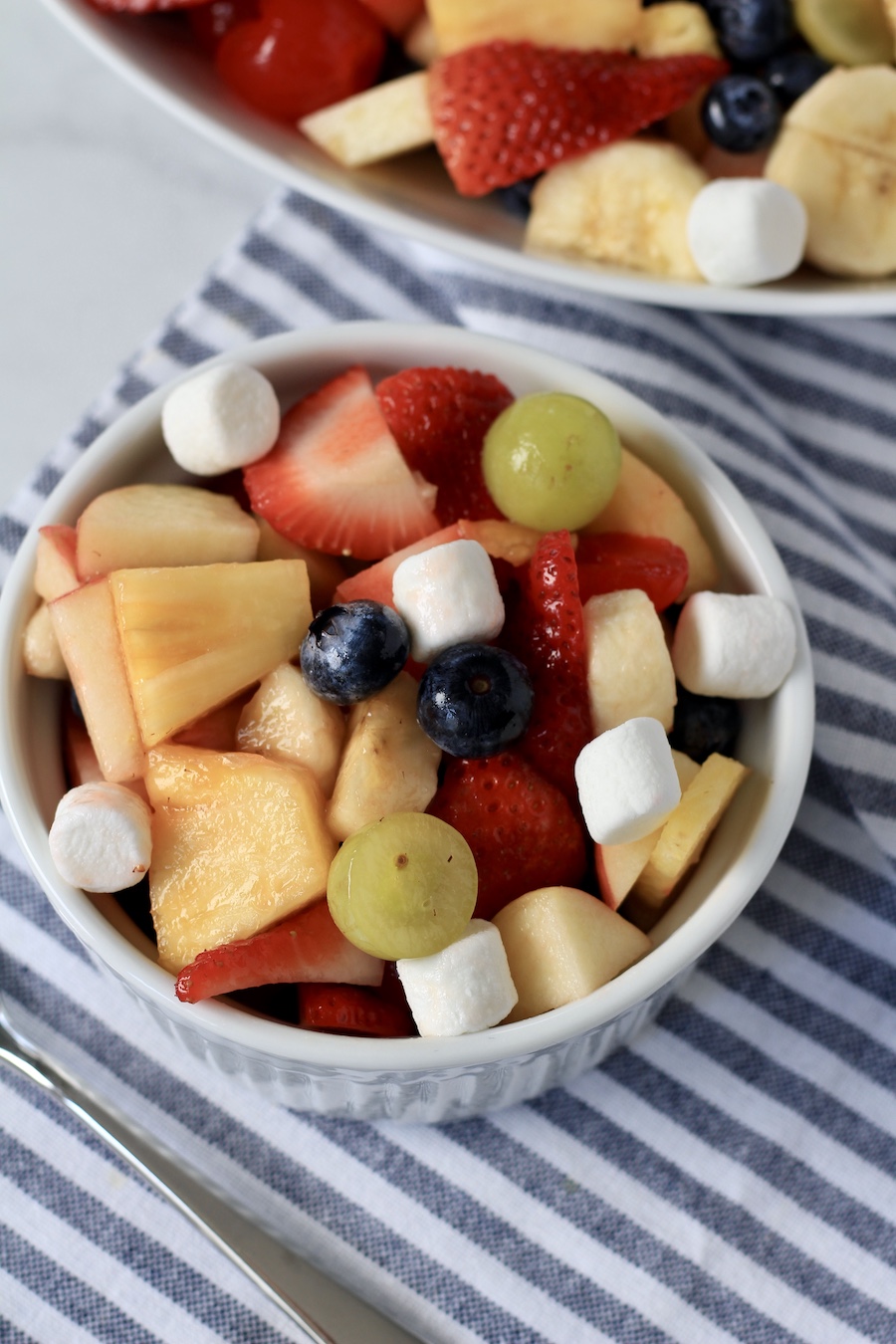 A top down photo of fruit salad on a white and blue striped towel.