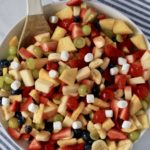 The full bowl of fruit salad topped with marshmallows on a white and blue towel.