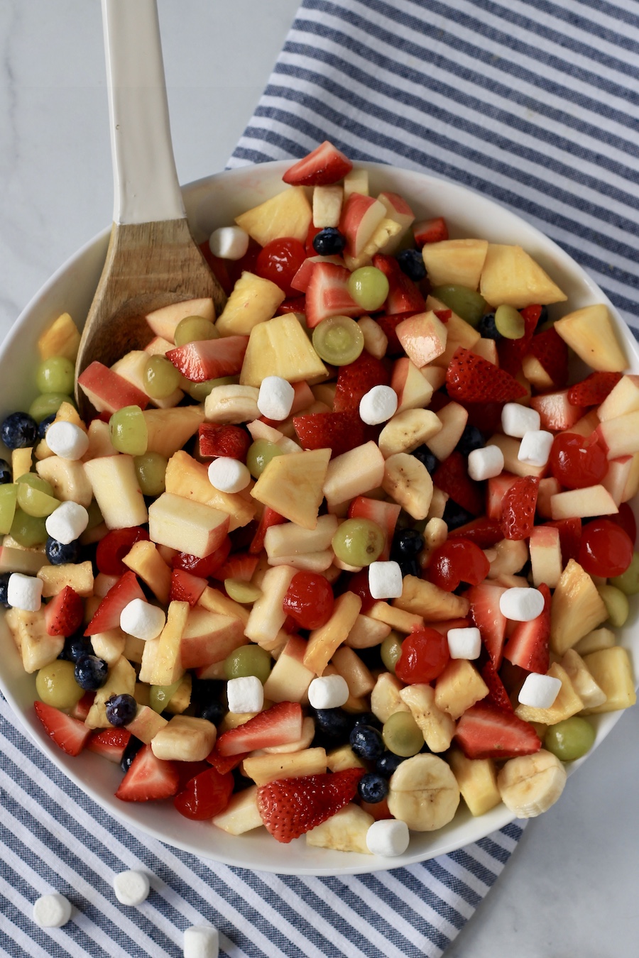 The full bowl of fruit salad topped with marshmallows on a white and blue towel.