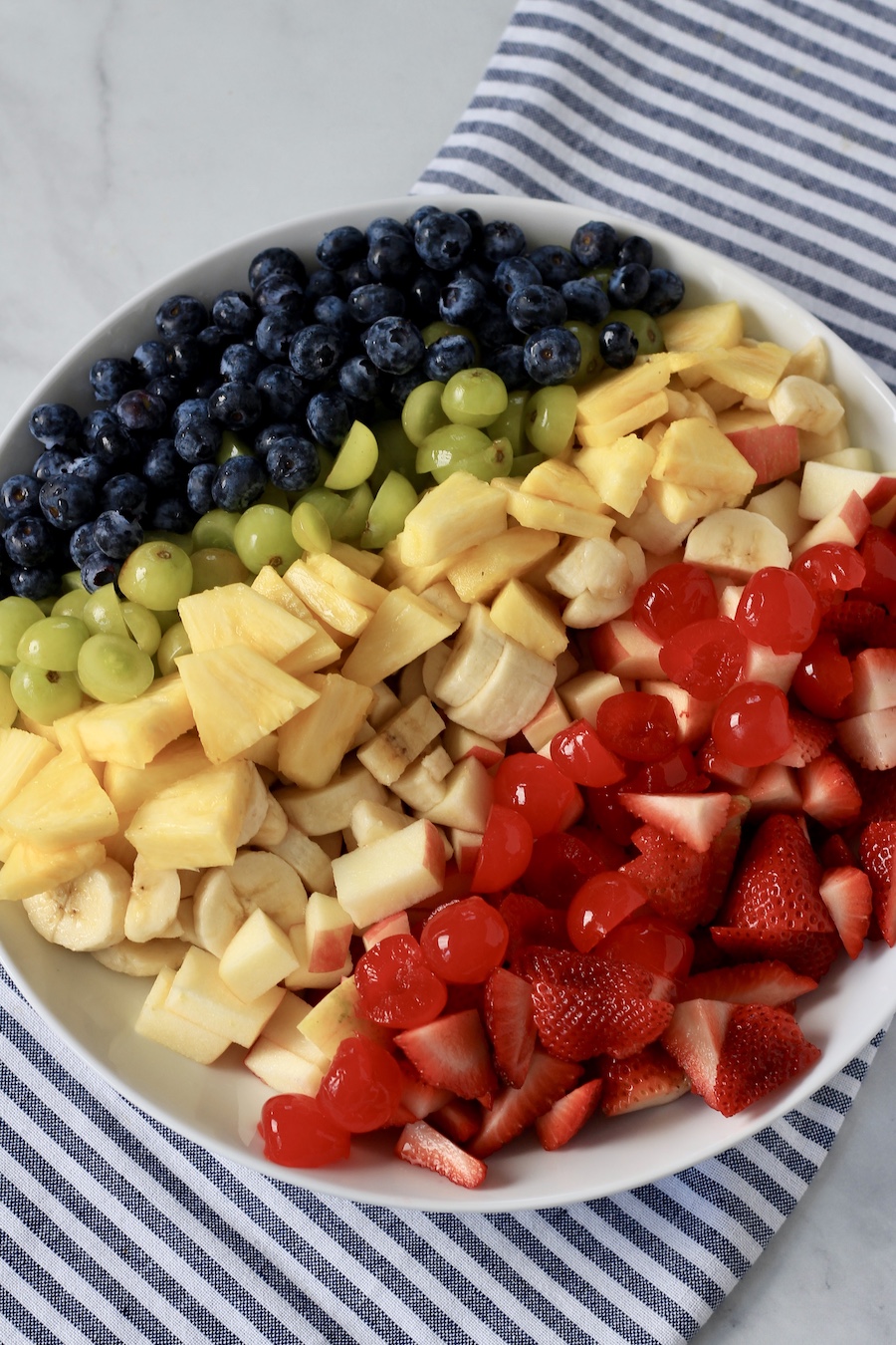 A white bowl with fruit in rainbow order on a blue and white towel.