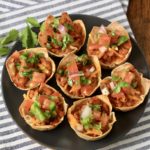 Taco cups topped with pico de gallo on a blue plate with cilantro on a white and blue towel.