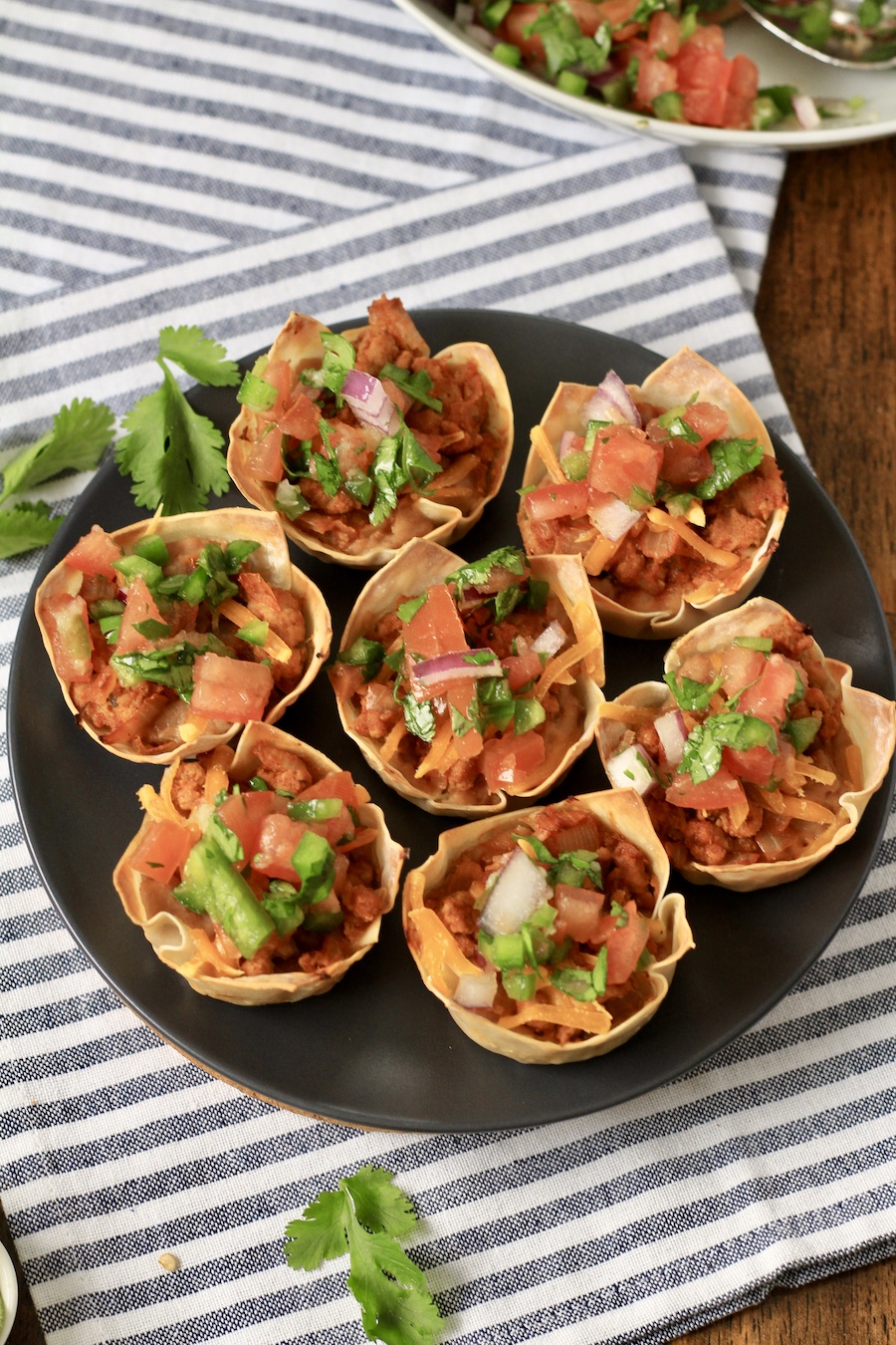 Taco cups topped with pico de gallo on a blue plate with cilantro on a white and blue towel.