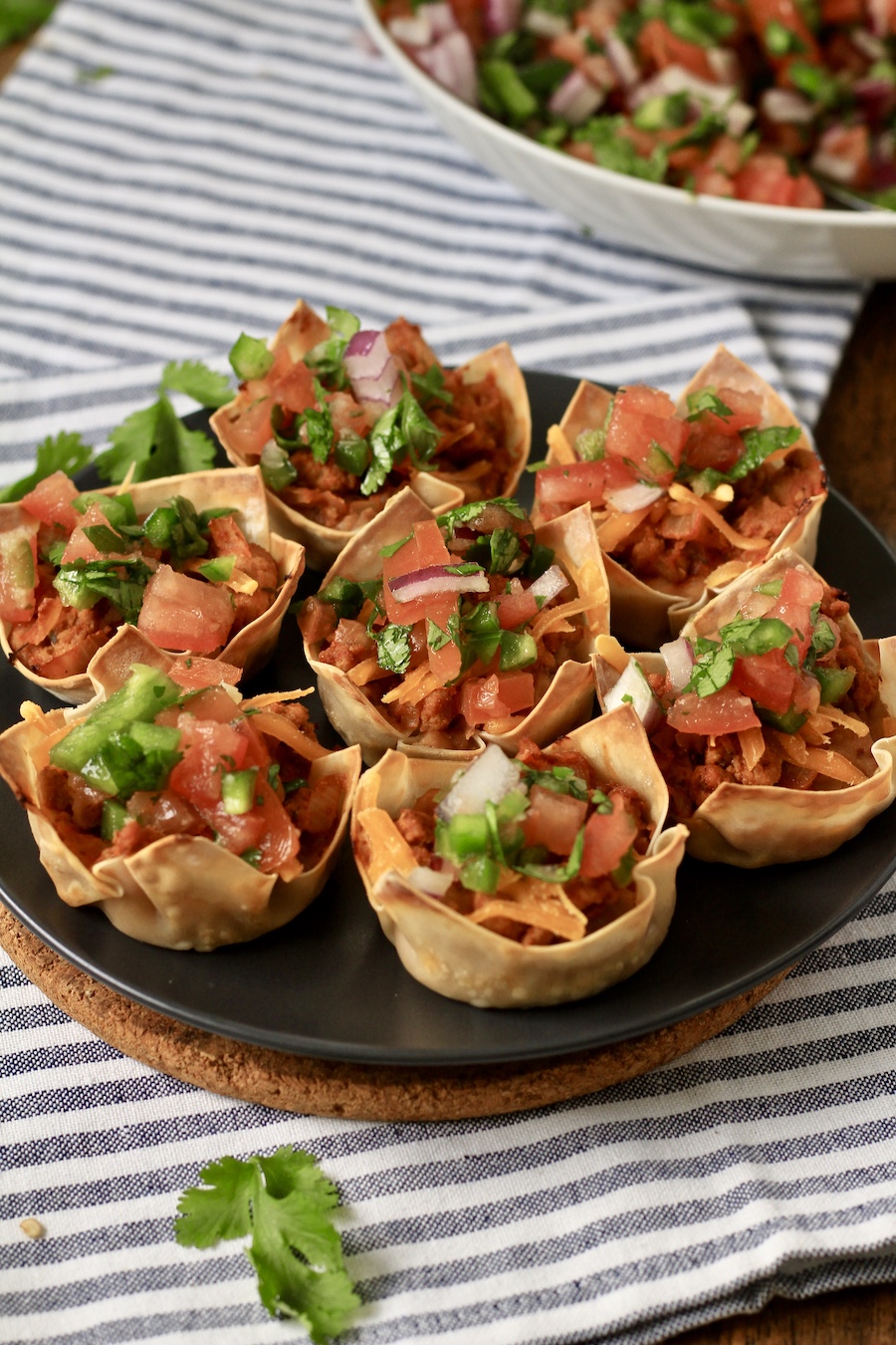 From the side, a blue plate with 7 taco cups topped with pico de gallo.