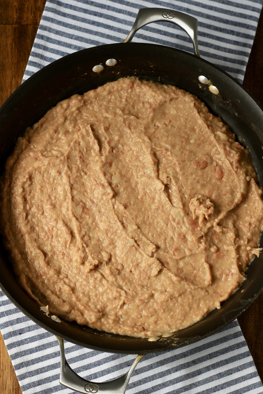 Creamy refried beans in a non-stick skillet on a white and blue dish towel.