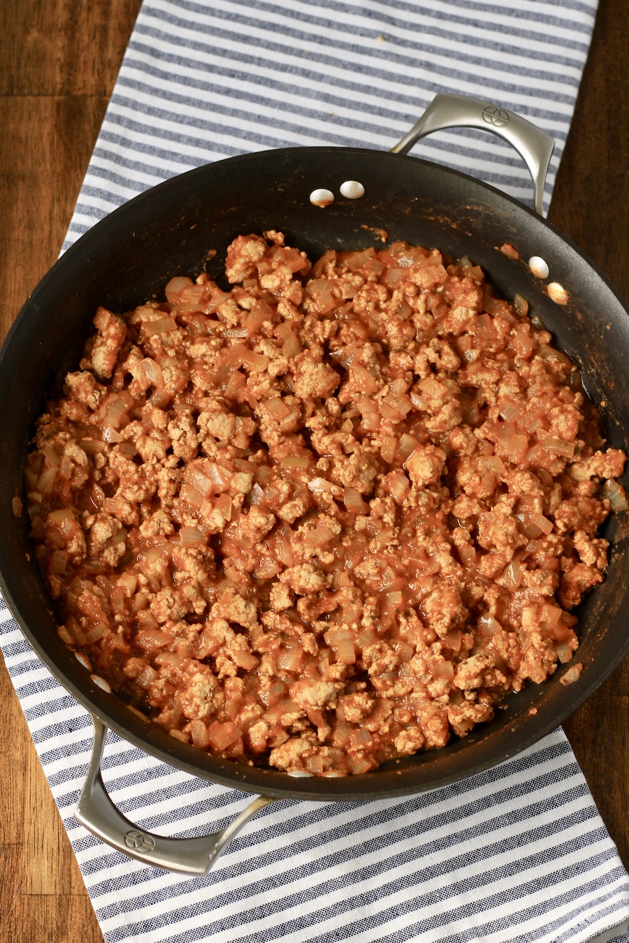 Taco meat after cooking in a non-stick skillet on a white and blue dish towel.